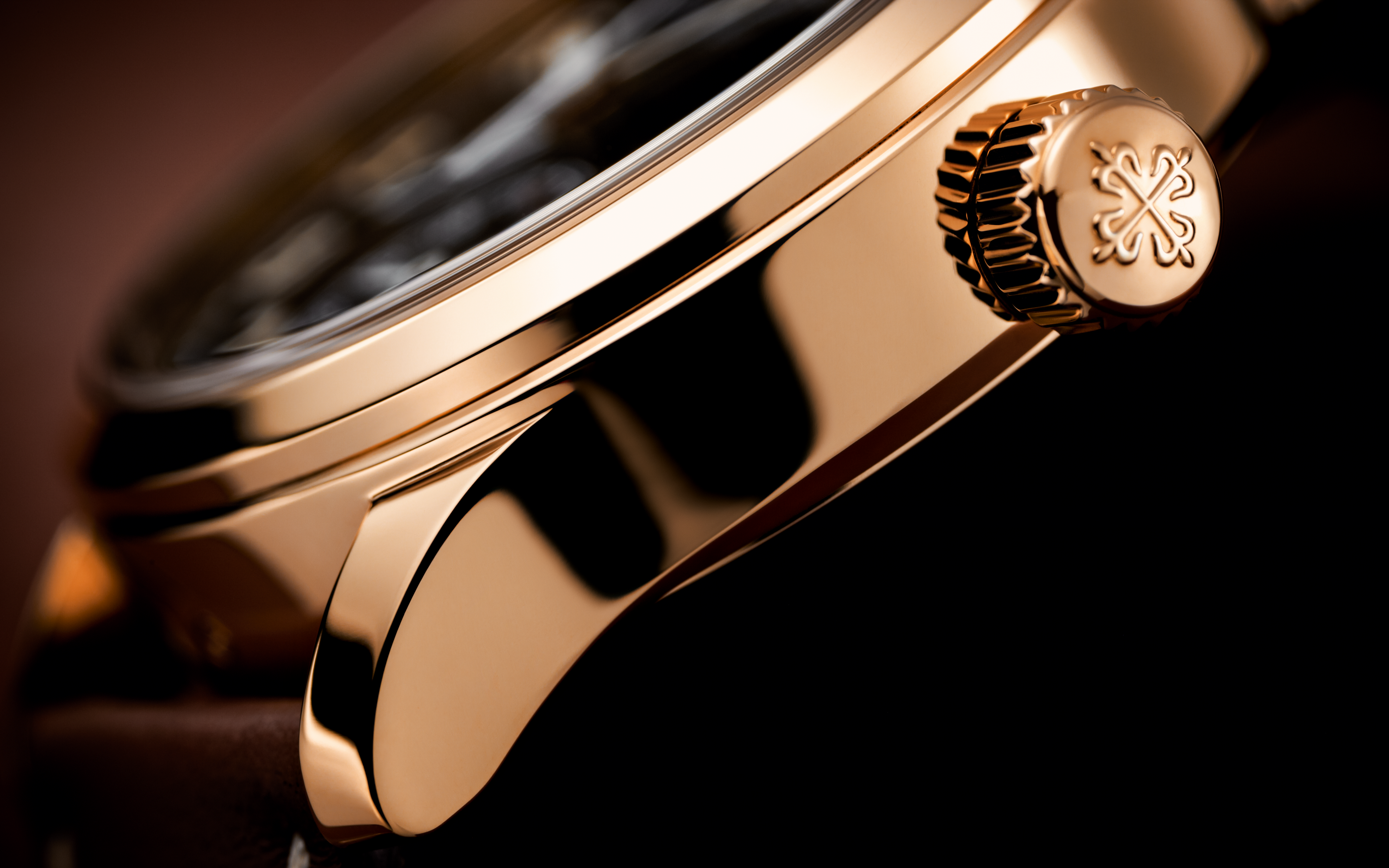 Close-up of a gold watch with a brand logo on a dark background