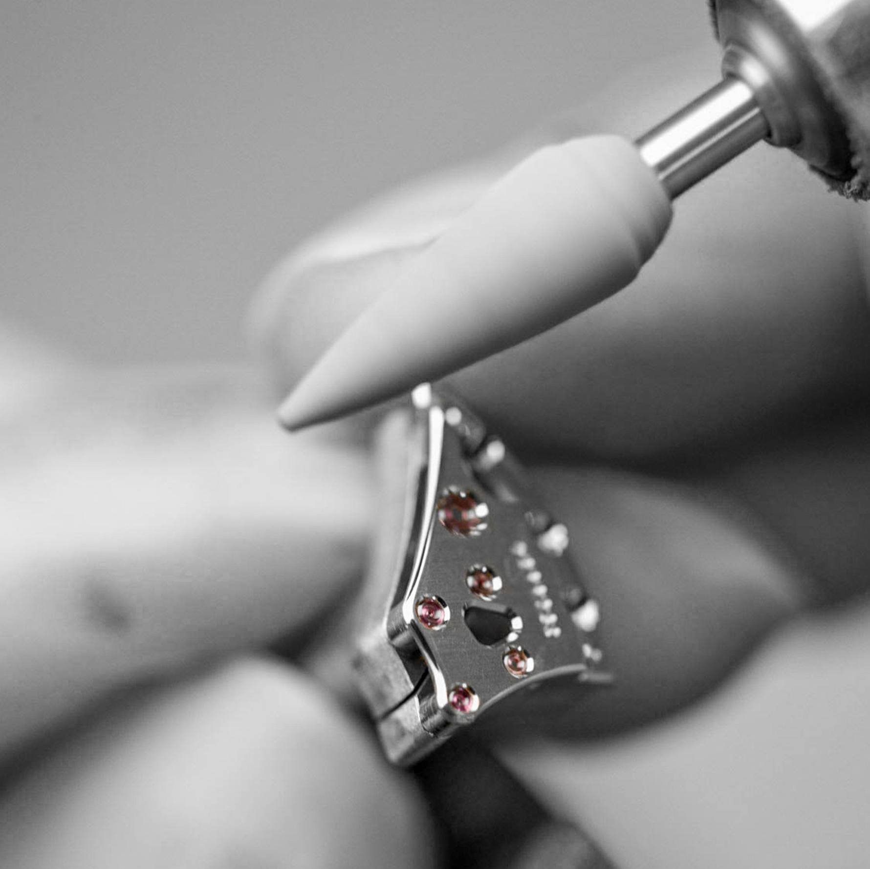 Close-up of a silver earring with pink gemstones being held by tweezers.